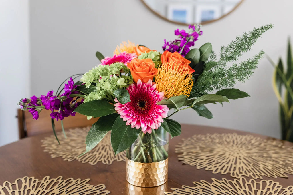 A vibrant tropical arrangement featuring a variety of colorful flowers in a vase, placed on a table with a patterned tablecloth.