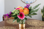 A vibrant tropical arrangement featuring a variety of colorful flowers in a vase, placed on a table with a patterned tablecloth.