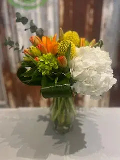 A floral arrangement featuring a variety of flowers including tulips, in a clear glass vase.