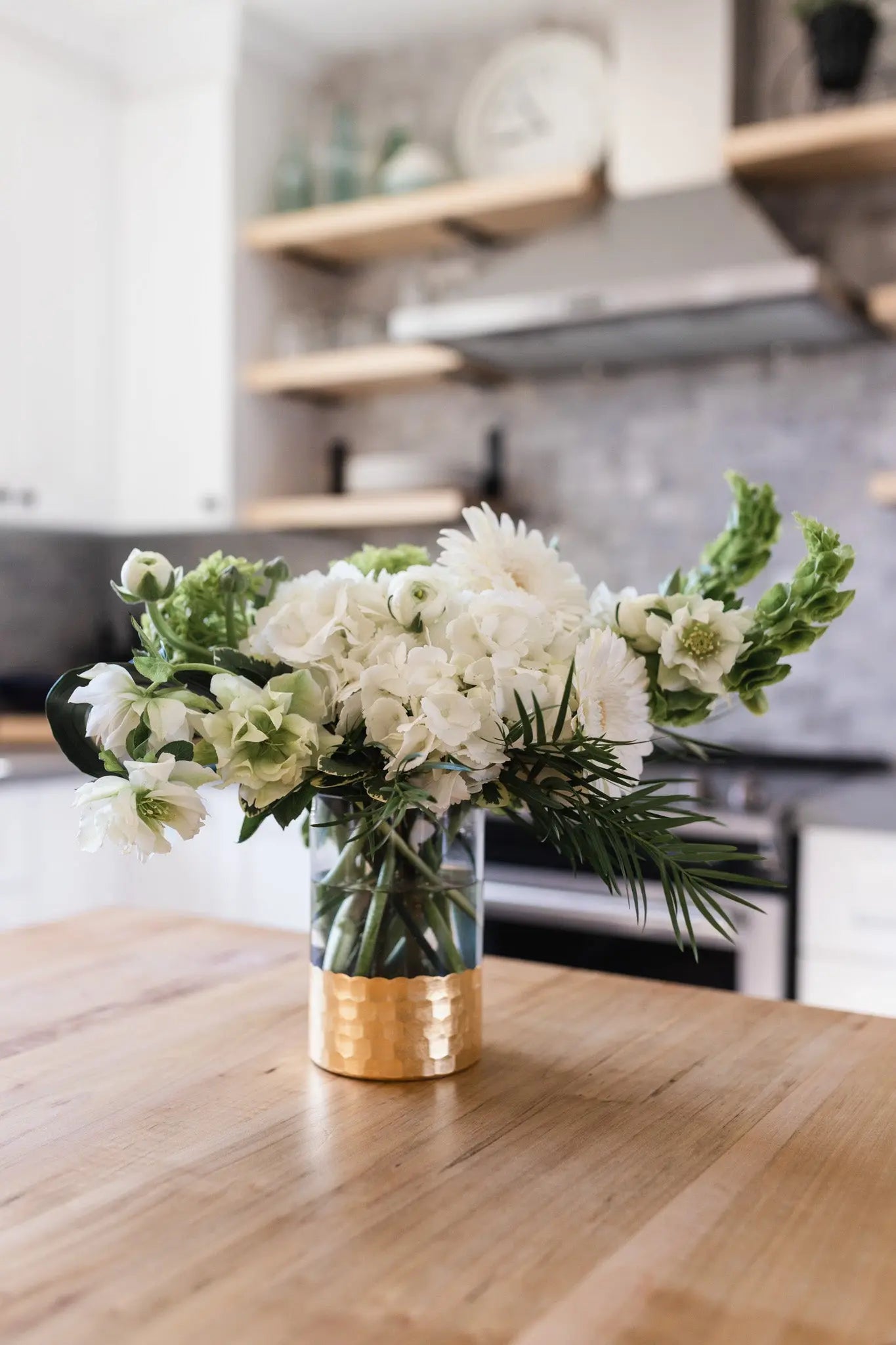 A white and green floral arrangement in a clear glass vase.